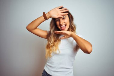 İzole arka planda rahat beyaz t-shirt giyen genç güzel bir kadın gülümseyen neşeli oyun Peek bir Boo elleri ile yüz gösteren. Sürpriz ve çıkıldı