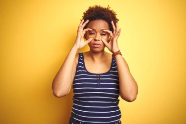Beauitul Afro-Amerikalı kadın izole edilmiş sarı arka plan üzerine yaz tişörtü giyiyor parmaklarıyla gözlerini açmaya çalışıyor, uykulu ve yorgun bir şekilde sabah yorgunluğu çekiyor.