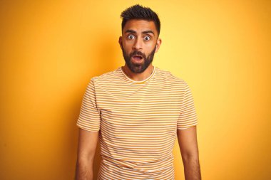 Sarı arka plan üzerinde duran genç bir Hintli tişört giyiyor. Şok olmuş yüz ifadesiyle, şüpheci ve alaycı görünüyor.