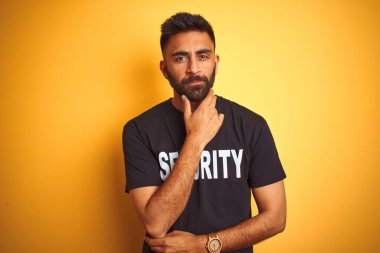 İzole edilmiş sarı arka plan üzerinde güvenlik üniforması giyen, kollarını kavuşturup gülümseyen ve çenesini kaldıran Arap Hintli İspanyol güvenlik görevlisi. Olumlu düşünüyorum..
