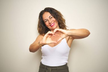 Orta yaşlı yaşlı bir kadın, izole edilmiş beyaz bir geçmişin başında durmuş, sevgiyle gülümsüyor ve elleriyle kalp sembolü ve şekli gösteriyor. Romantik konsept.