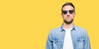 Yüzünde ciddi bir ifade ile moda güneş gözlüğü giyen yakışıklı adam. Basit ve doğal kamera bakıyor.