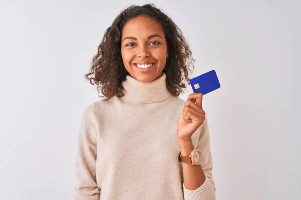若いですブラジル人女性保持クレジットカードスタンディング上の隔離された白い背景に幸せな顔立ちと笑顔で自信を持って笑顔示す歯 — ストック写真
