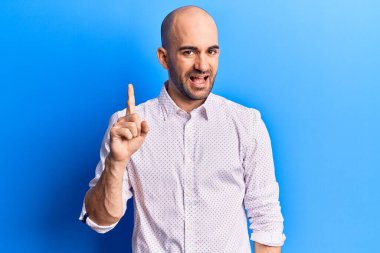 Zarif bir tişört giymiş genç yakışıklı kel bir adam bir fikir veya soruyla gülümsüyor ve mutlu bir yüzle işaret ediyor. 