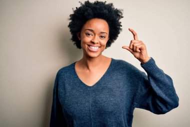 Kıvırcık saçlı, sıradan bir süveter giyen, el hareketleriyle küçük beden işareti yapan ve kameraya bakan güzel Afro-Amerikan bir kadın. Ölçü kavramı.