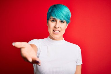 Mavi saçlı, kırmızı arka planda rahat tişörtler giyen genç ve güzel bir bayan dostça bir selamlama ve hoş geldin hediyesi olarak el sıkışmayı sunuyor. Başarılı bir iş..