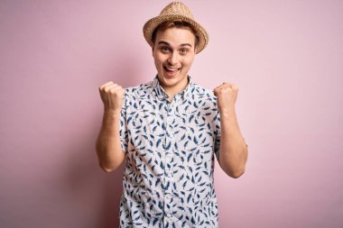 İzole edilmiş pembe arka plan üzerinde gündelik gömleği ve şapkası olan yakışıklı kızıl saçlı adam kollarını kaldırarak ve açık gözlerle başarıyı kutluyor ve şaşırıyor. Kazanan konsept.