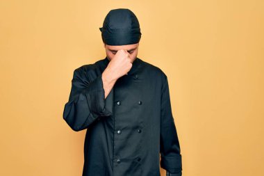 Mavi gözlü, üniformalı ve sarı arka planda şapka takan yakışıklı fırıncı yorgun burnu ve gözleri ovuşturup yorgun ve baş ağrısı çekiyor. Stres ve hüsran kavramı.