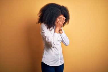 Afro saçlı, güzel Afro-Amerikan zarif bir kadın. Sarı arka planda duruyor. Ağlarken suratını ellerle kapatıyor. Depresyon kavramı.