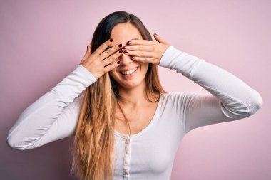 Genç, sarışın, mavi gözlü, pembe arka planda beyaz tişört giyen, elleri gülücüklü ve komik olan güzel bir kadın. Kör kavram.