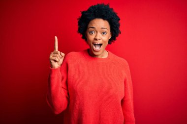 Young beautiful African American afro woman with curly hair wearing casual sweater pointing finger up with successful idea. Exited and happy. Number one.
