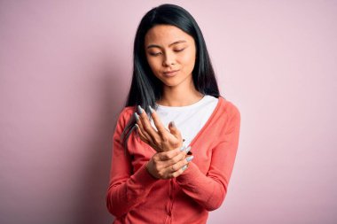 İzole edilmiş pembe arka plan üzerine sıradan süveter giyen genç, güzel Çinli bir kadın. Ellerinde ve parmaklarında ağrılar, iltihaplanma.