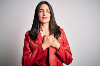 Genç esmer, mavi gözlü, beyaz arka planda kırmızı bir ceket giyen, elleri göğsünde, gözleri kapalı ve yüzünde minnet dolu bir jest olan bir kadın. Sağlık kavramı.