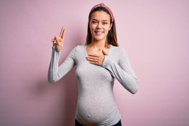 Young beautiful teenager girl pregnant expecting baby over isolated pink background smiling swearing with hand on chest and fingers up, making a loyalty promise oath clipart
