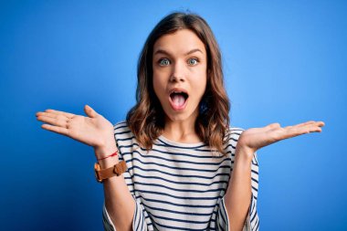 Mavi izole edilmiş arka planda dikilip kollarını kaldırıp heyecanla haykırarak başarıyı kutlayan genç, güzel sarışın kız. Kazanan konsept