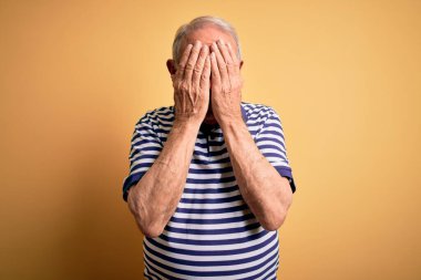 Gri saçlı, donanma çizgili tişört giyen, sarı arka planda duran, ağlarken yüzünü ellerle kapatan son sınıf öğrencisi. Depresyon kavramı.