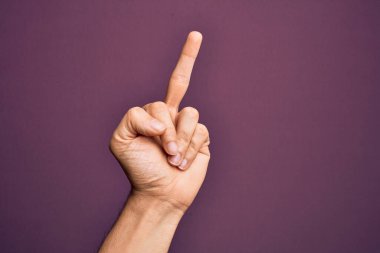 Hand of caucasian young man showing fingers over isolated purple background showing provocative and rude gesture doing fuck you symbol with middle finger