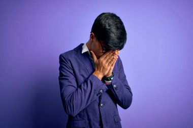 Ceket ve gözlük takan yakışıklı genç bir iş adamı. Mor arka planda, üzgün bir yüz ifadesi var. Ağlarken yüzünü kapatıyor. Depresyon kavramı.