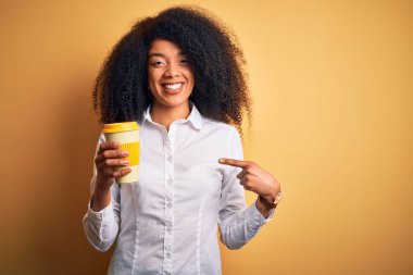 Afro saçlı, kahve içen Afro-Amerikalı genç bir iş kadını. Elinle ve parmağınla mutlu bir şekilde işaret ediyor.