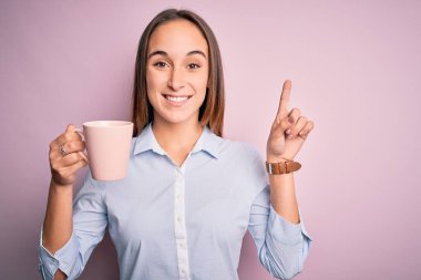 Genç ve güzel bir kadın izole edilmiş pembe arka planda duran kahve fincanı içerken bir fikir ya da soru işareti ile şaşırdı.