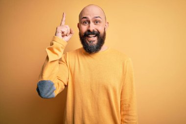 Sarı arka planda dikilmiş sakallı yakışıklı kel adam başarılı bir fikirle parmağını kaldırıyor. Heyecanlı ve mutlu. Bir numara..