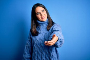 Mavi gözlü, balıkçı yaka kazak giyen genç, esmer bir kadın. Gülümsüyor, yardım eli uzatıyor ve kabul ediyor..