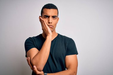 Genç, yakışıklı, Afro-Amerikalı bir adam beyaz arka planda dikilen sıradan bir tişört giyiyor. Kollarını kavuşturup depresyondan sıkılmış ve yorgun görünüyor..