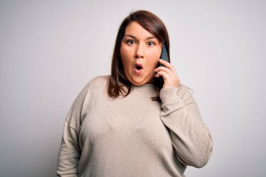 Güzel ve cüsseli bir kadın akıllı telefondan konuşuyor. Arka planda izole bir şekilde konuşuyor. Şaşırmış bir yüz ifadesinden korkuyor ve heyecanlanıyor.