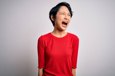 Genç, güzel Asyalı bir kız, gündelik kırmızı tişört giyip izole edilmiş beyaz arka plan üzerinde öfkeli ve öfkeli bir şekilde bağırıyor. Öfke ve agresif kavram.