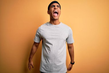 Yakışıklı Afro-Amerikan sporcu sarı arka plan üzerine spor giysisi giyiyor kızgın ve öfkeli çığlıklar atıyor, öfkeyle bağırıyor. Öfke ve agresif kavram.