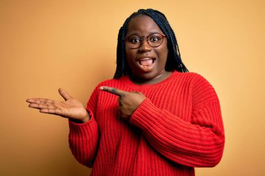 Sarı arka planda normal süveter giyen Afro-Amerikan kadın elini uzatarak ve parmağını göstererek kameraya bakıp hayrete düştü..