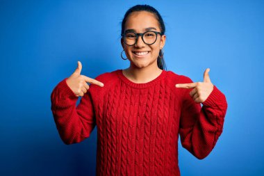Mavi arka planda günlük süveter ve gözlük takan genç, güzel Asyalı bir kadın. Kendine güvenen, yüzünde gülümseme olan, kendini gururlu ve mutlu gösteren bir kadın..