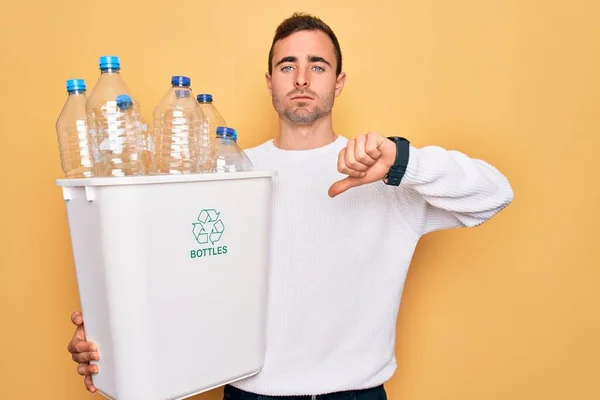 青い目をした若いハンサムな男は怒った顔をしたプラスチックボトルで財布を保持リサイクル 親指で嫌いを示す負のサインダウン 拒否の概念 — ストック写真