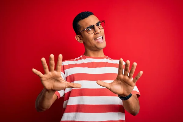 年轻英俊的非洲裔美国男子 身穿休闲条纹T恤 戴着眼镜 害怕恐惧地表情 用手停止手势 震惊地大叫 恐慌的概念 — 图库照片