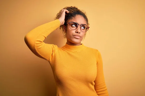 黄色の背景の上にセーターと眼鏡を身に着けている若い美しいアフリカ系アメリカ人の少女は混乱し 疑問に思います 疑いもなく 頭の上で手で考えて 包括的概念 — ストック写真