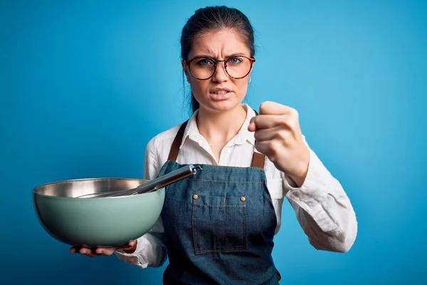 若いです美しいです炊飯器の女性と青い目を使用してボウルと泡立て器隔離された背景にイライラし 怒りで叫びます クレイジーと上げ手で叫んで 怒りの概念 — ストック写真