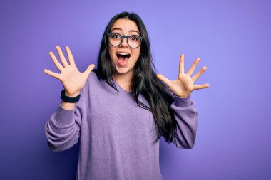 Mor izole edilmiş arka planda gözlük takan genç esmer kadın çılgın ve başarıyı kollarını kaldırıp heyecanla haykırarak kutluyor. Kazanan konsept