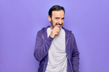 İzole edilmiş arka planda sıradan mor bir kazak giyen, kolları çapraz ve çenesi açık kameraya bakarak gülümseyen orta yaşlı yakışıklı bir adam. Olumlu düşünüyorum..