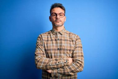 Yüzünde ciddi bir ifadeyle mavi arka planda duran günlük gömlek ve gözlük takan genç yakışıklı bir adam. Basit ve doğal bir şekilde kameraya bakıyorsun..