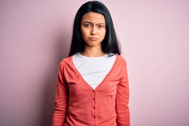 Genç, güzel, Çinli bir kadın pembe arka planda rahat bir süveter giyiyor. Depresyonda ve sıkıntıdan endişe ediyor. Kızgın ve korkmuş. Üzücü ifade.