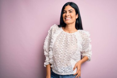 Moda kıyafetleri giyen genç ve güzel bir kadın. Manken, sokak tarzı giyiniyor. Pembe arka planda dikiliyor.