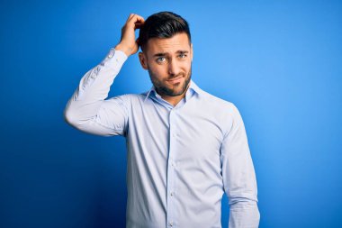 Soyutlanmış mavi arka plan üzerinde duran zarif gömlekli genç yakışıklı adam soru sormayı merak ediyor. Şüpheyle kararsız, kafa kafaya düşünerek. Düşünceli kavram.