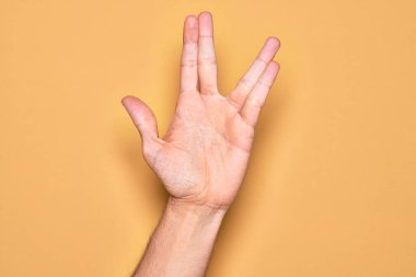 Kafkasyalı genç adam parmaklarını izole edilmiş sarı arka planda gösteriyor. Vulkan selamı veriyor, el ve parmaklarını gösteriyor, ucube kültürü sergiliyor.