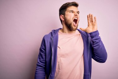 Sakallı, mavi gözlü, pembe arka planda mor eşofman üstü giyen, el ele tutuşup bağıran genç sarışın bir adam. İletişim konsepti.