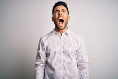 Zarif gömlekli genç adam izole edilmiş beyaz arka planda öfkeli ve öfkeli bir şekilde bağırıyor. Öfkeyle bağırıyor. Öfke ve agresif kavram.