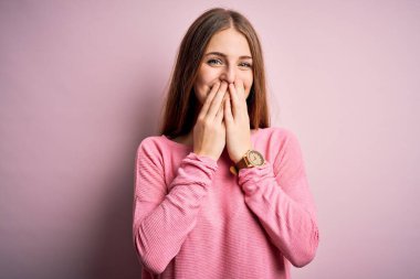 Genç, güzel, kızıl saçlı bir kadın pembe arka planda rahat bir süveter giyiyor. Gülüyor ve utanıyor. Ağzı ellerle, dedikoduyla ve skandal konseptiyle örtüyor.