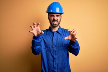 Sakallı tamirci mavi üniformalı ve sarı arka planda kasklı komik bir şekilde gülümseyen kedi, agresif ve seksi bir ifade takınıyor.