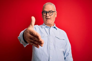 Orta yaşlı, yakışıklı, beyaz bir adam kırmızı arka planda günlük çizgili gömlek ve gözlük takıyor. Dostça bir selamlama ve hoş geldin hediyesi olarak gülümsüyor. Başarılı bir iş..