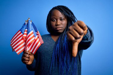 Genç vatansever Afro-Amerikalı örgülü kadın elinde kızgın yüzlü Birleşik Devletler bayrakları, olumsuz işaretler baş parmakları aşağıda, reddedilme kavramı