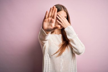 Genç, güzel, kızıl saçlı bir kadın pembe arka planda gözlük ve süveter takıyor, gözleri ellerle örtüyor ve üzgün ve korku ifadeleriyle jest yapıyor. Utanç verici ve olumsuz bir kavram..